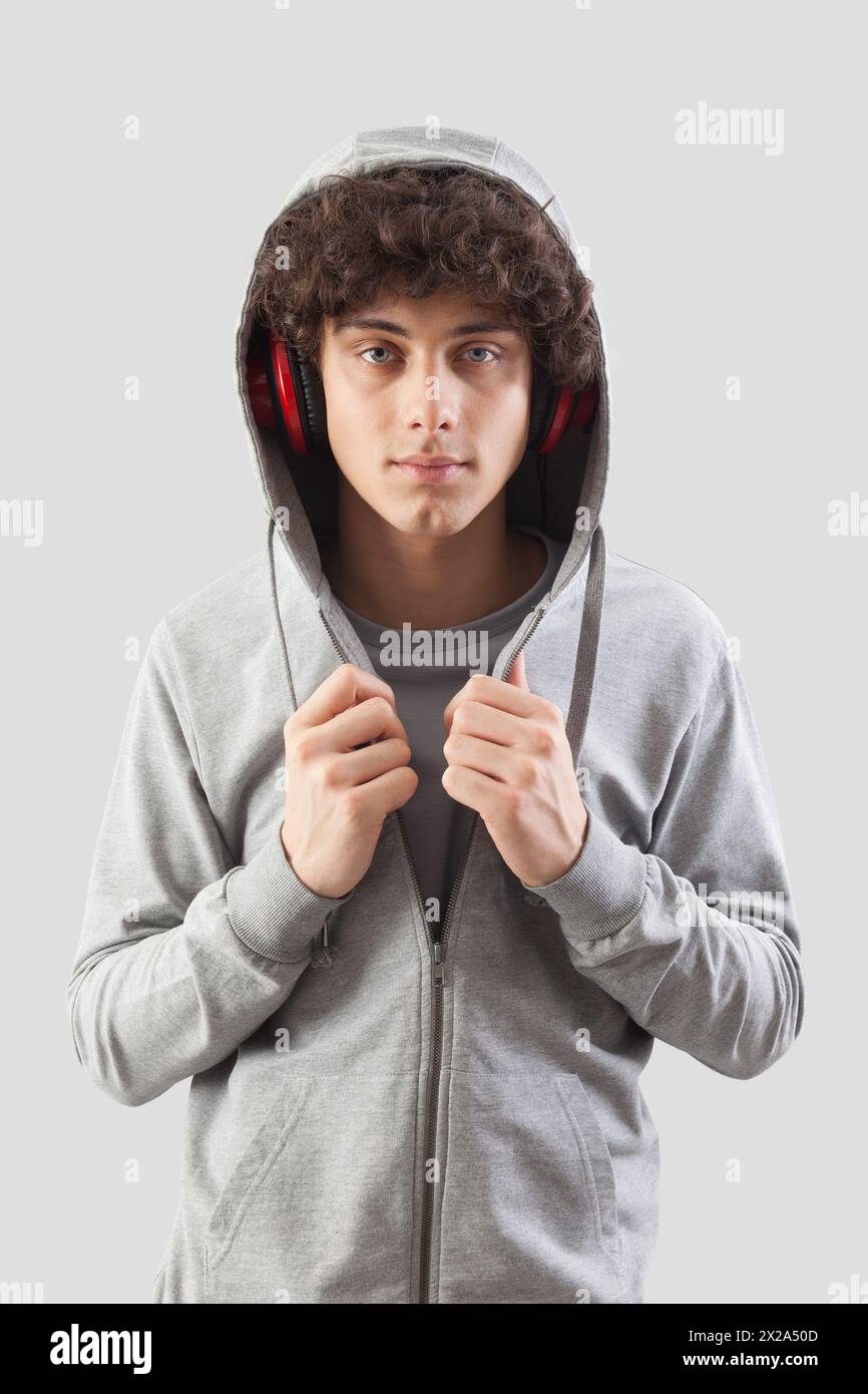 Handsome young man wears headphones and a hoodie sweatshirt and is isolated against a gray background. He looks into the camera with his blue eyes whi Stock Photo