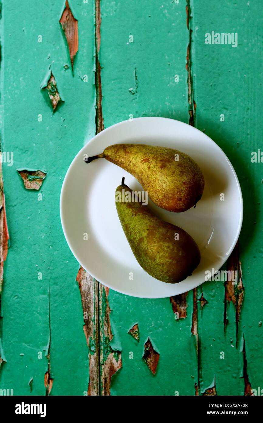 Two green pears on a white plate. Top view photo of an old wooden table. Healthy eating concept. Stock Photo