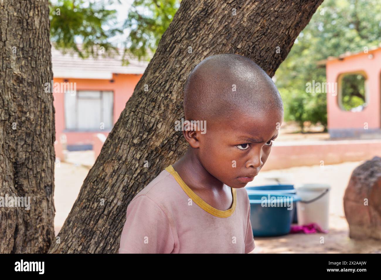 abused upset village african child, hiding behind a tree, standing in front of the house, Stock Photo
