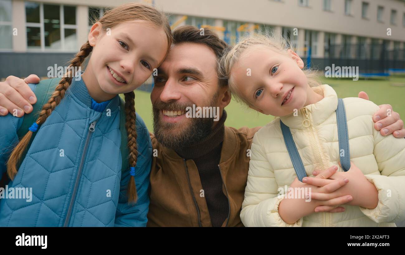 Father and two daughters looking at camera smiling laughing happy family parenting love joy elementary school learners schoolgirls pupils offspring Stock Photo