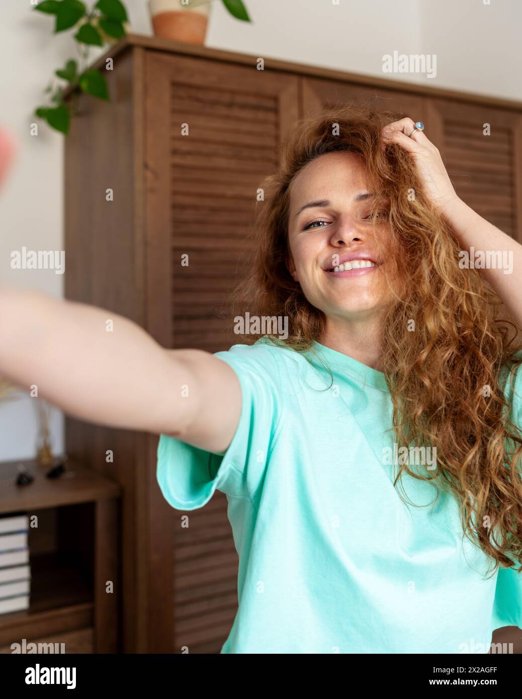 Attractive curly woman takes a selfie at home. Real life. Positive emotions. Self-admiration. Stock Photo