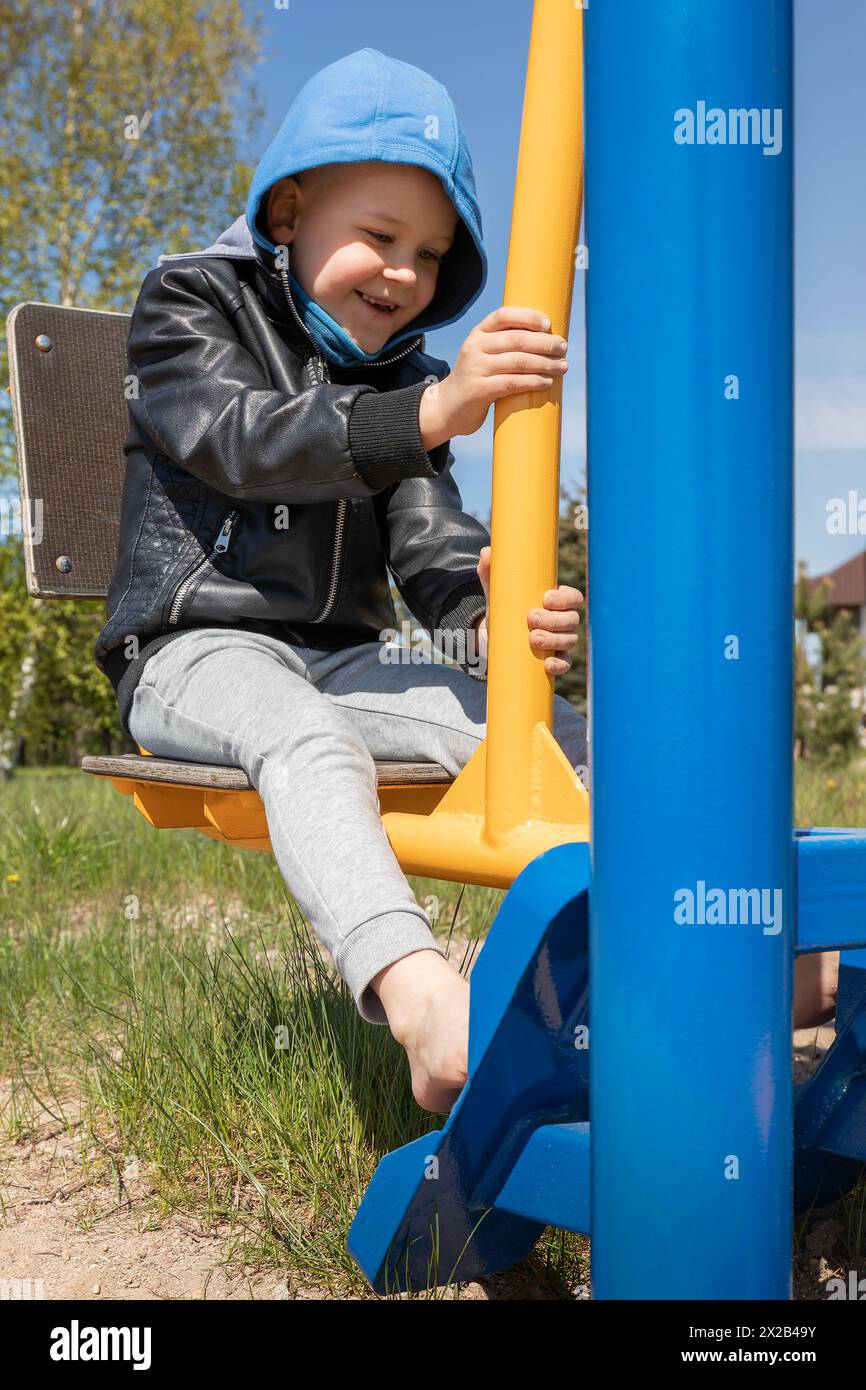 A smiling boy learns to do exercises on a leg press outdoor trainer. Stock Photo