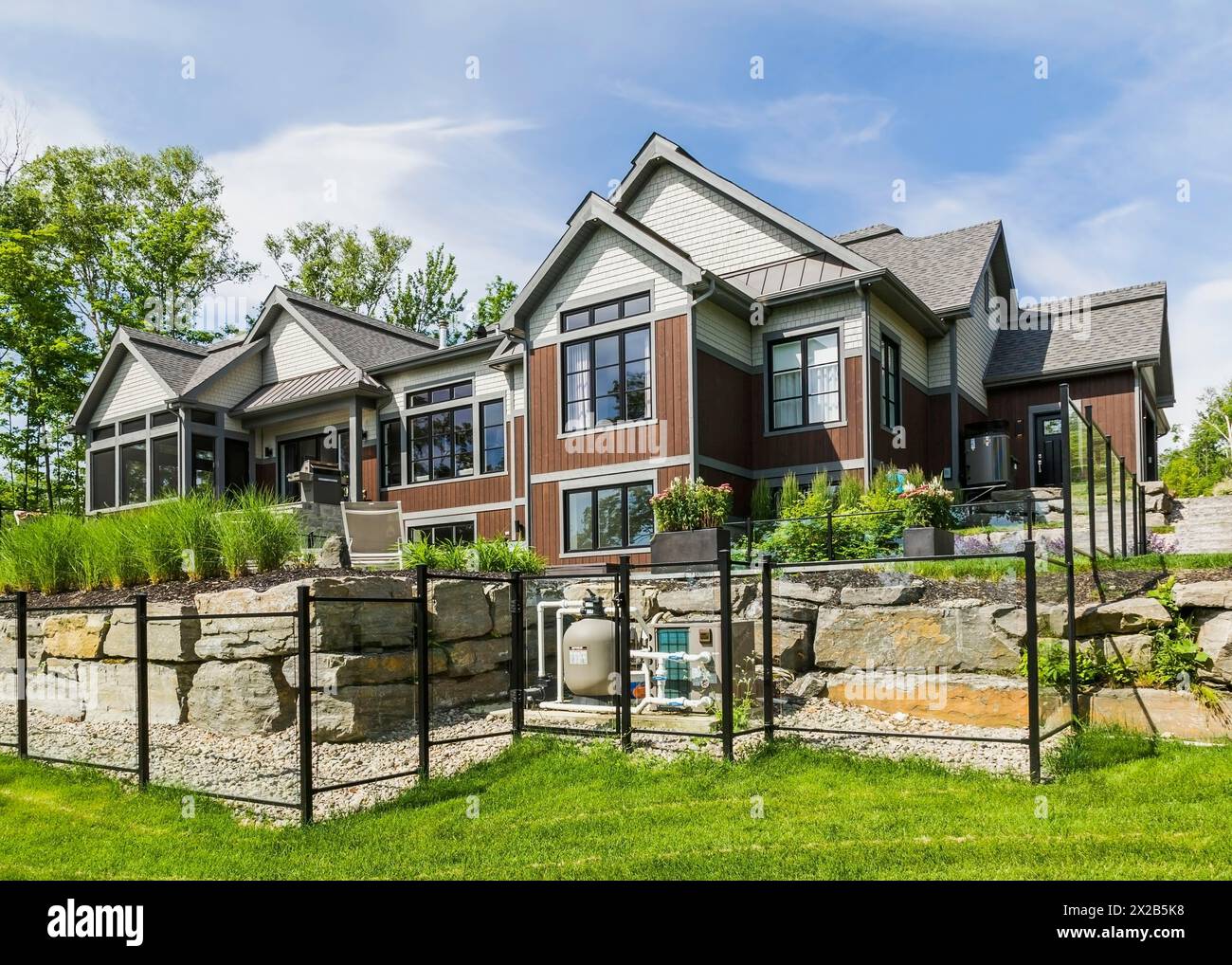 Rear view of contemporary natural stone and brown stained wood and cedar shingles clad luxurious bungalow style home in summer, Quebec, Canada, North Stock Photo