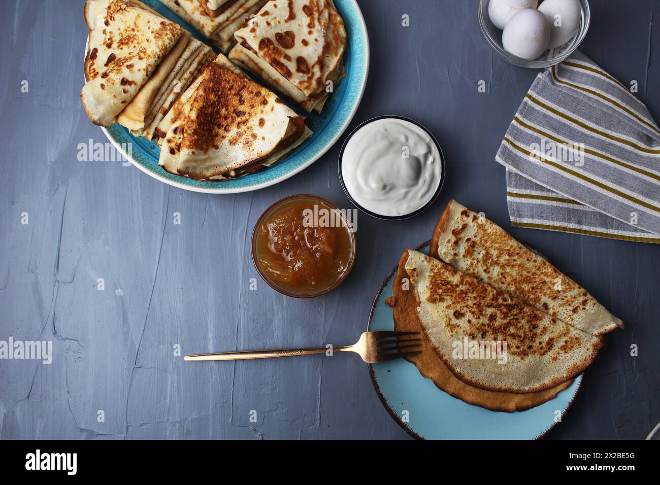 Still life top view breakfast concept pancakes crepe on dish and plate with fork next to it in gravy boat sour cream jam Stock Photo