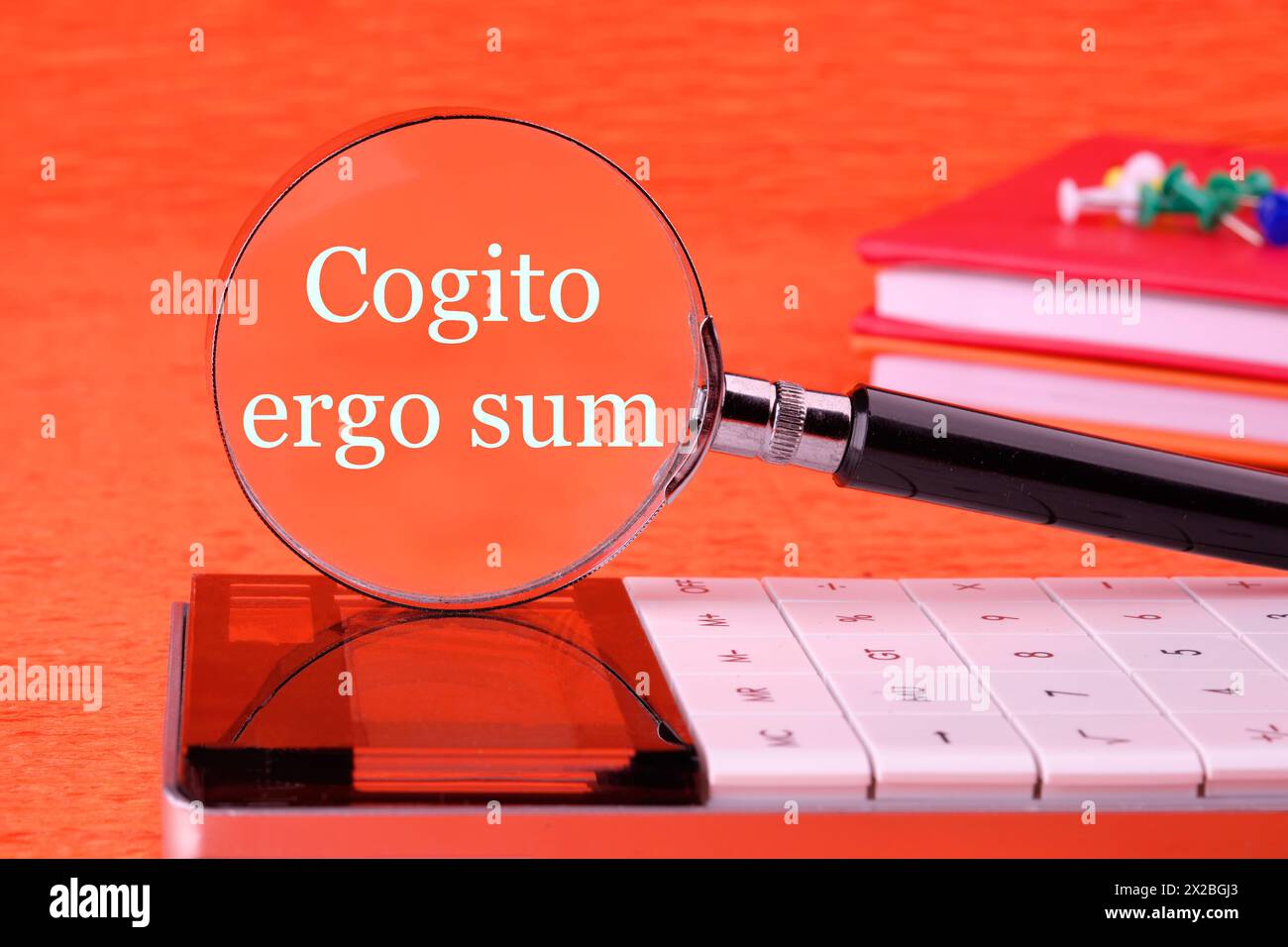 The words Cogito Ergo Sum or I think Therefore I Am through a magnifying glass in white font on an orange background Stock Photo