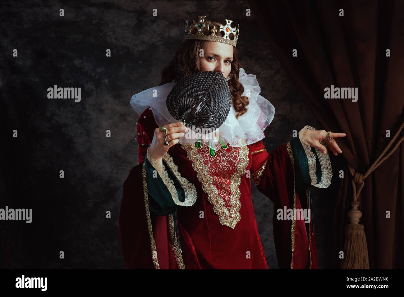 medieval queen in red dress with fan, white collar and crown on dark ...