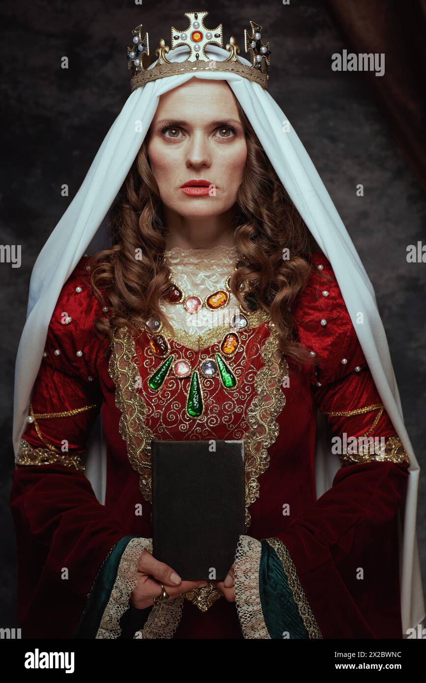 medieval queen in red dress with book, veil and crown on dark gray ...