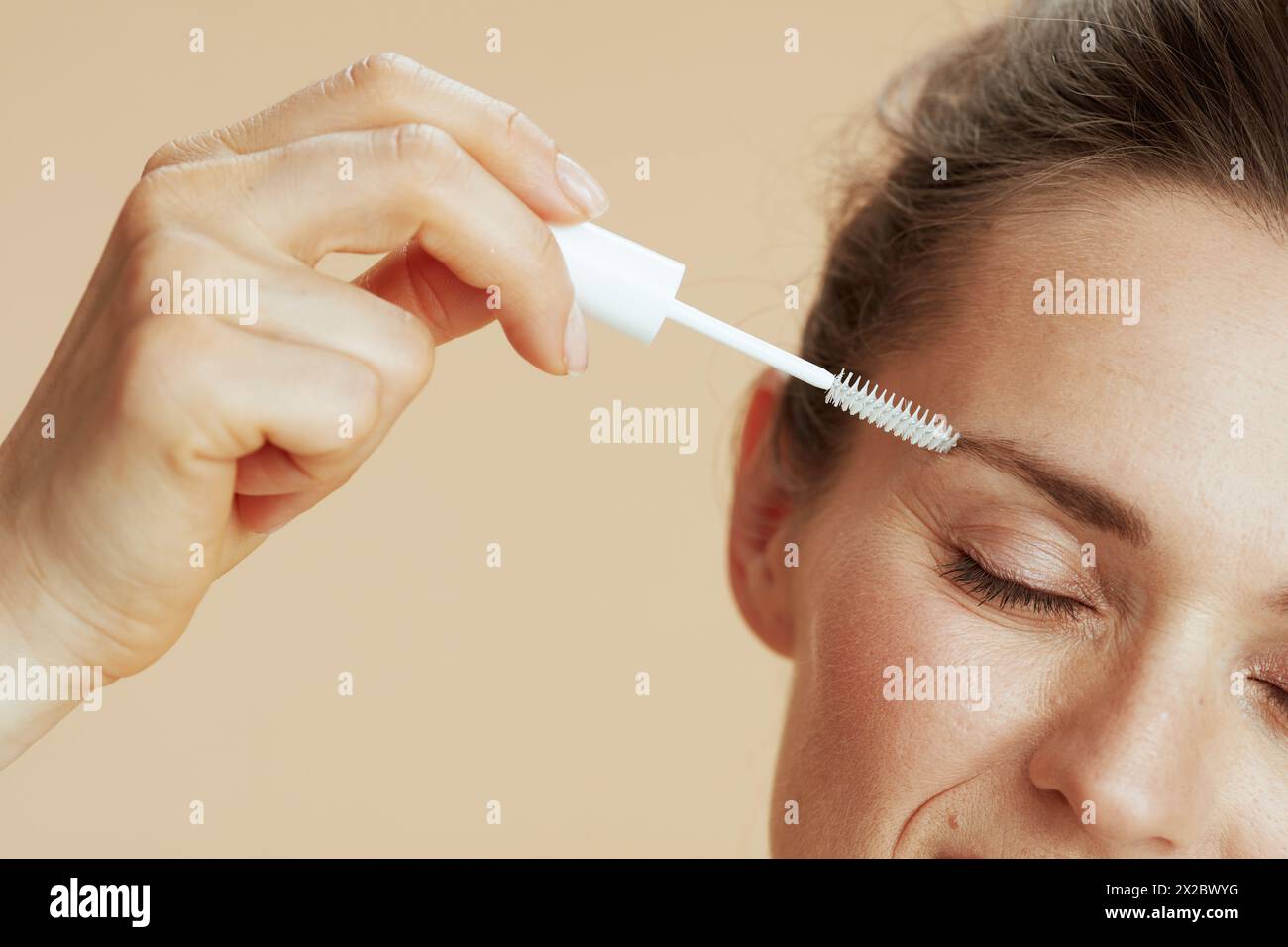 Closeup on middle aged woman with brow brush against beige background. Stock Photo