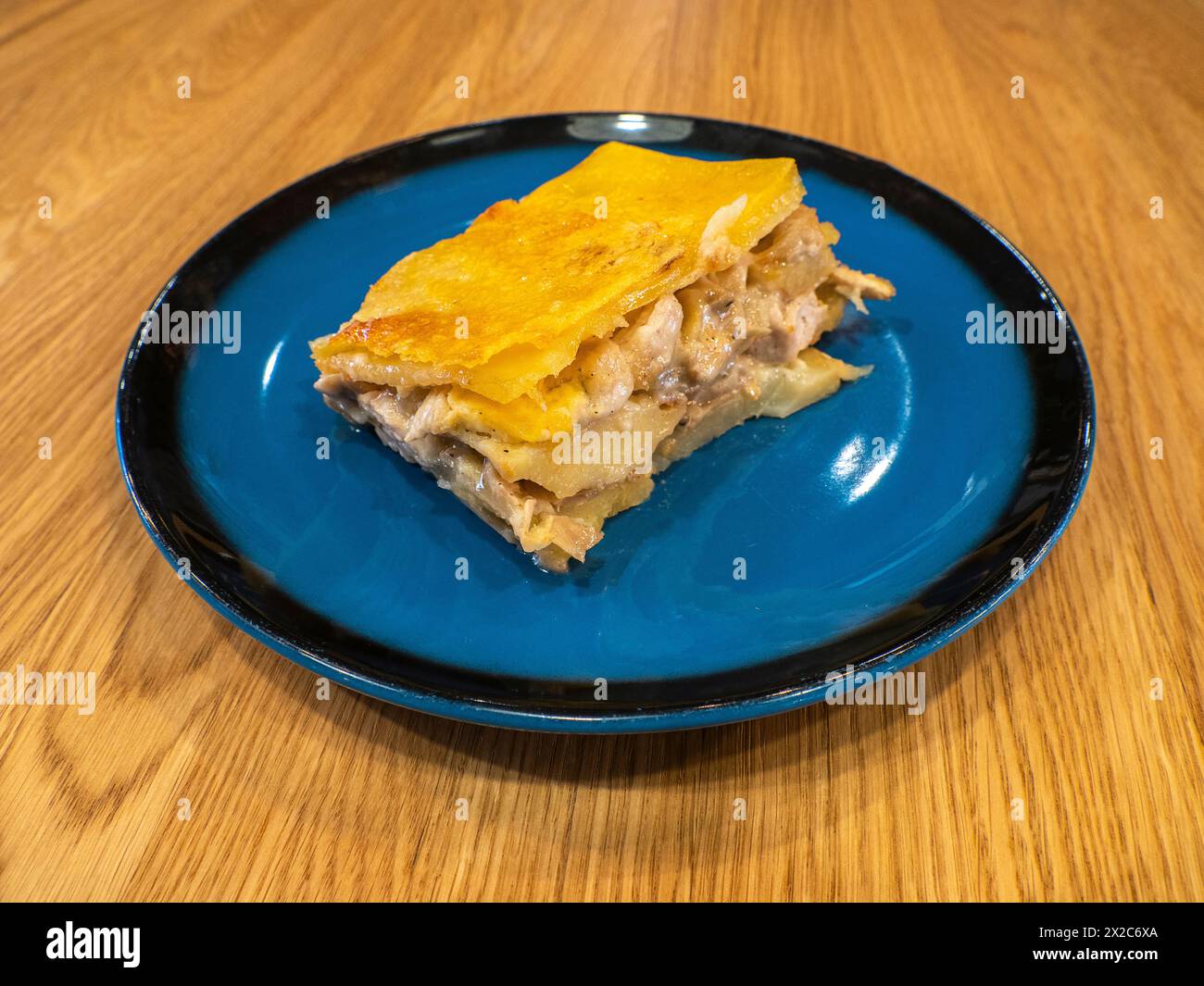 A piece of Potato casserole with mushrooms and chicken covered by cheese crust on the dark blue plate Stock Photo