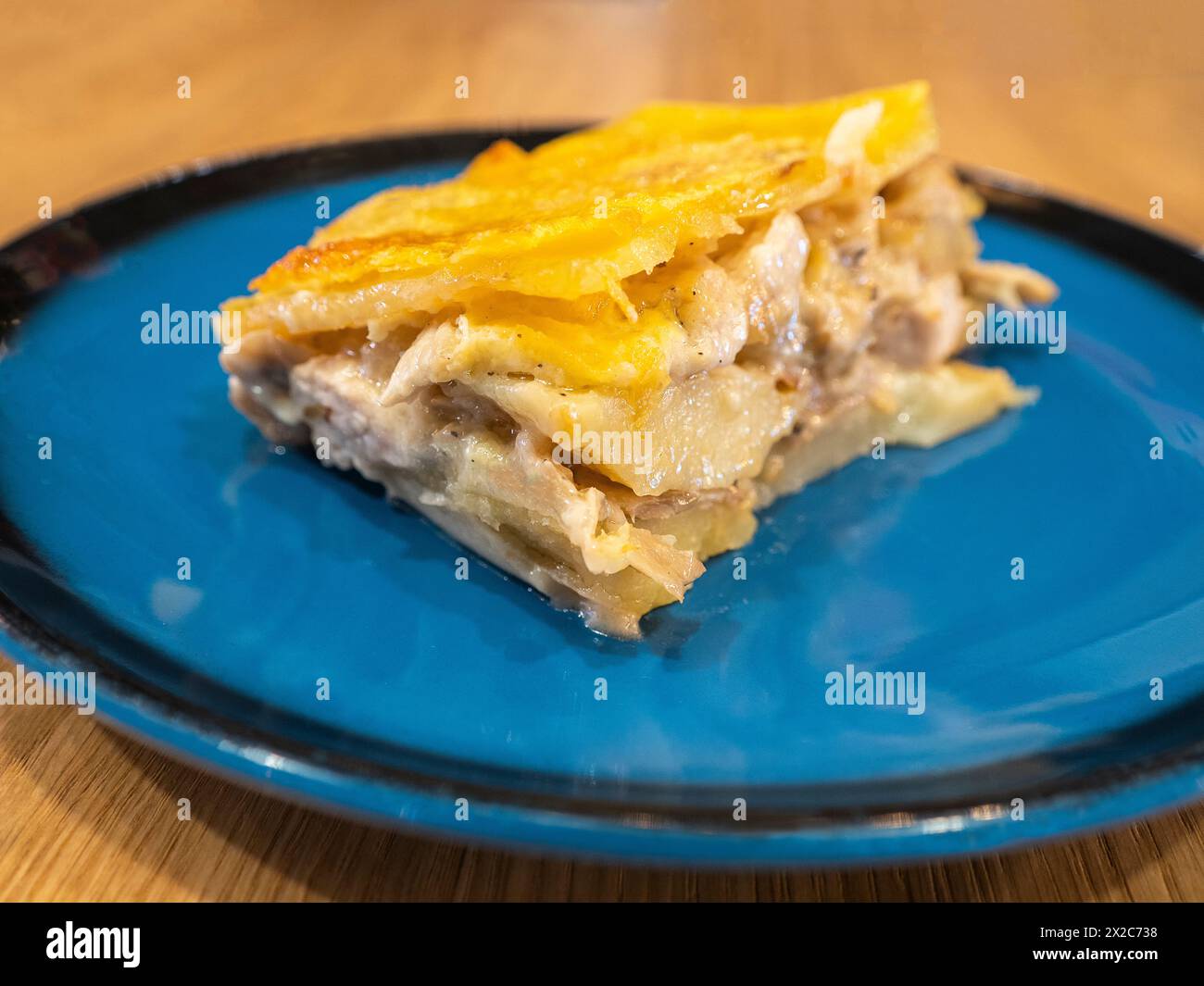 A piece of Potato casserole with mushrooms and chicken covered by cheese crust on the dark blue plate Stock Photo