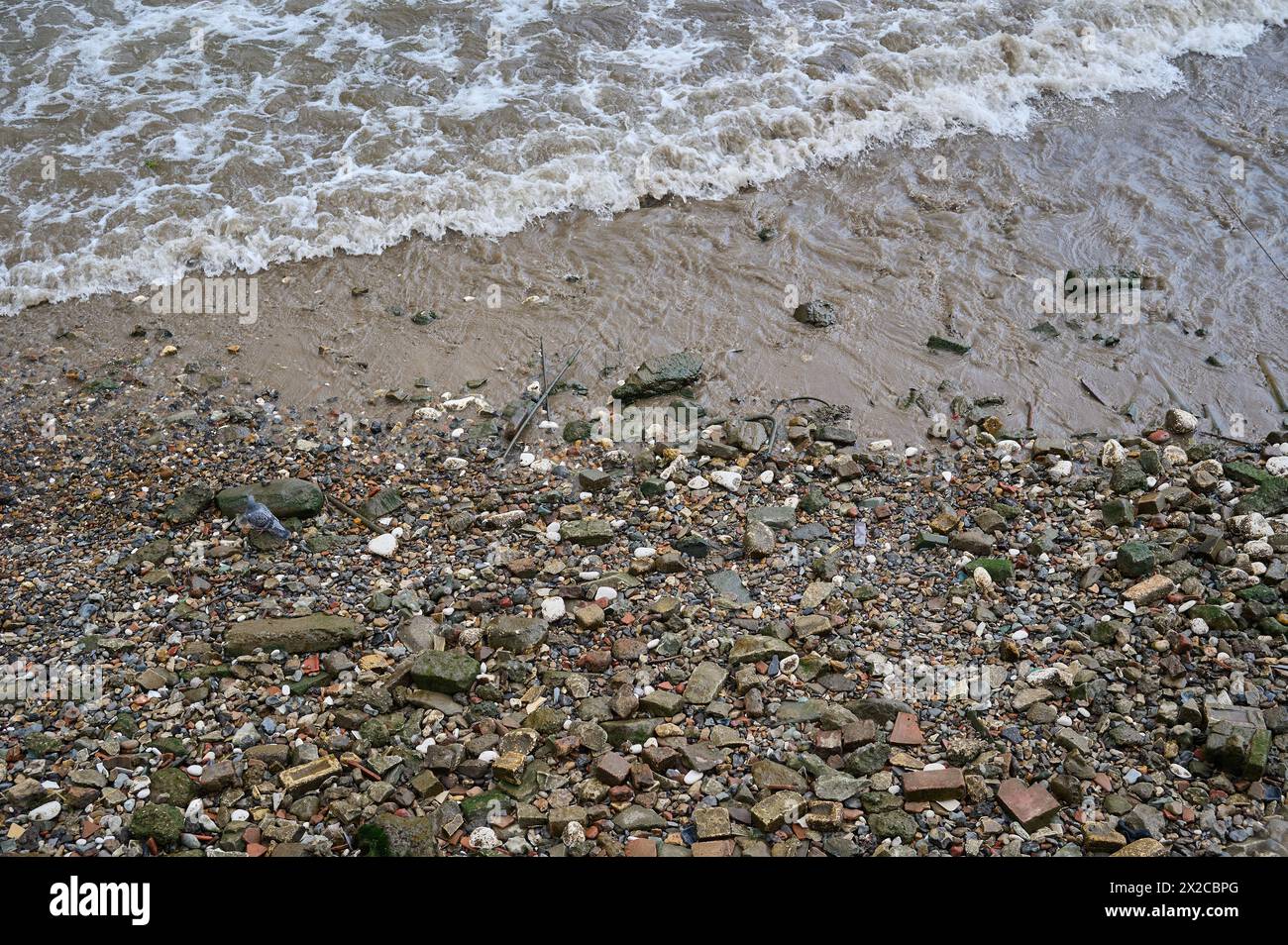 Looking down at small waves breaking on rocks and stones on river bank at low tide Stock Photo