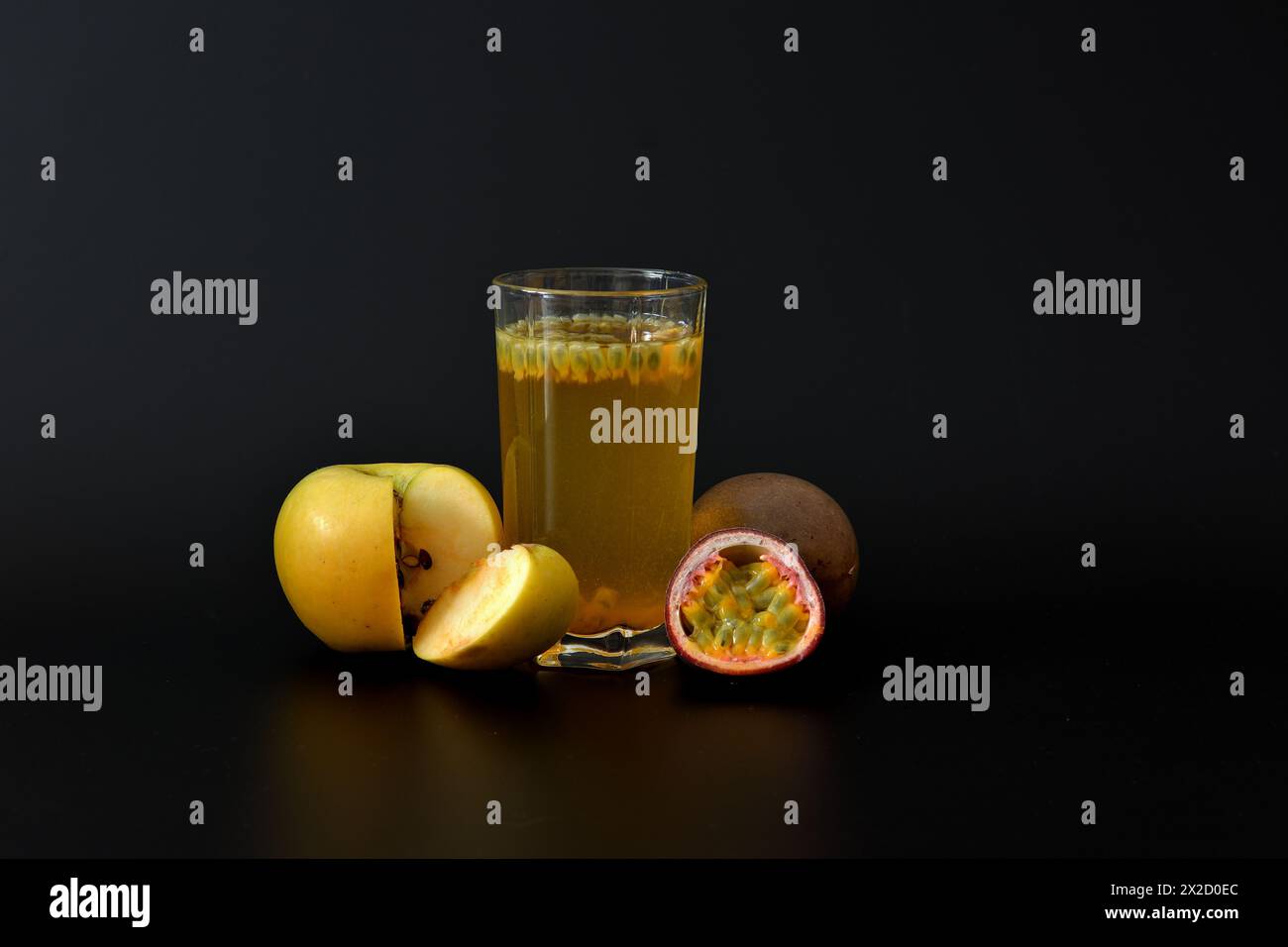A glass of fruit juice on a black background with seeds and slices of ripe green apple and chopped passion fruit. Close-up. Stock Photo