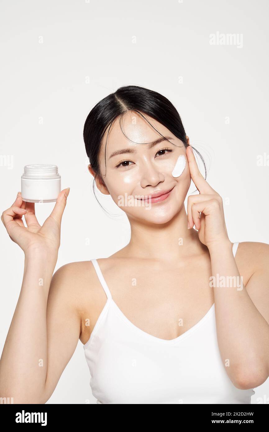 an Asian woman who holds a cream container and applies cosmetics to her face Stock Photo