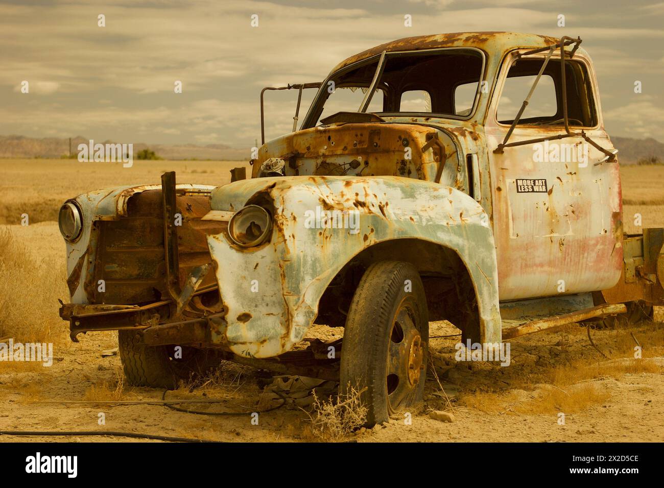 Close on an antique Chevy pickup truck, sun-scorched and abandoned, left sinking into the desert soil. Stock Photo