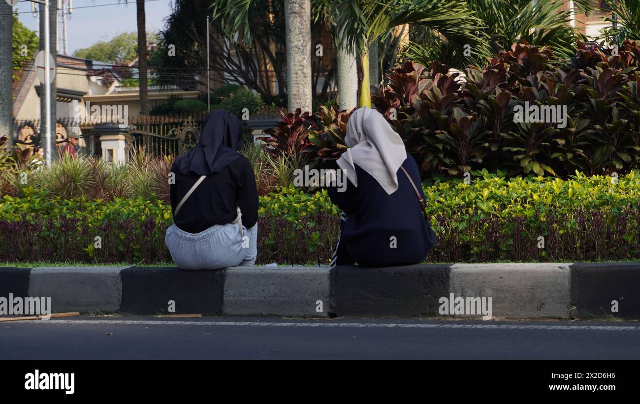 Two women wearing hijab sitting on the sidewalk facing the park to rest Two women wearing hijab sitting on the sidewalk facing the park to rest