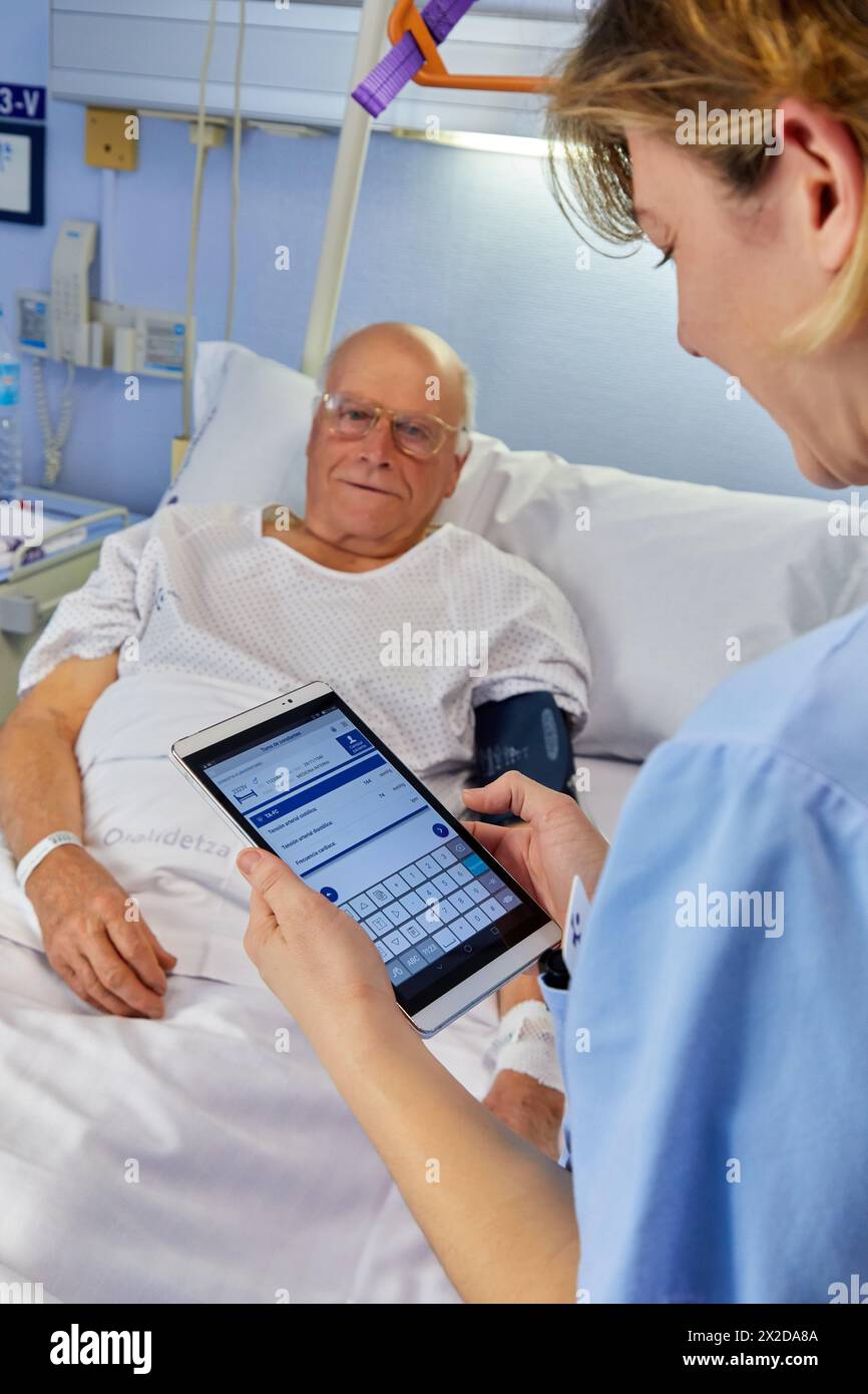 Nurse entering data of a patient on the tablet, hospital room, Hospital Donostia, San Sebastian, Gipuzkoa, Basque Country, Spain Stock Photo