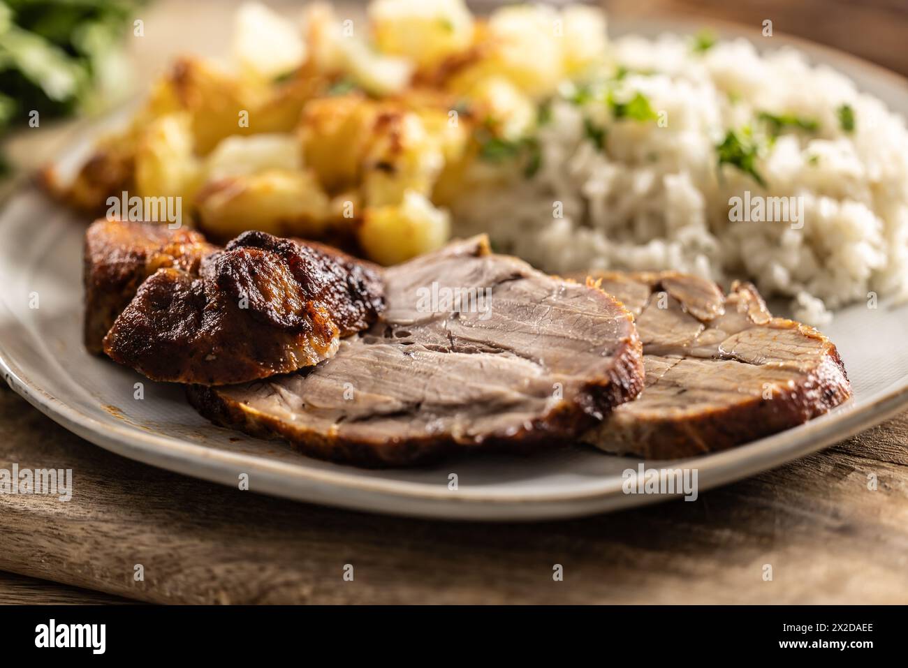 Slices of roasted neck with potatoes and rice on a plate - Close up. Stock Photo