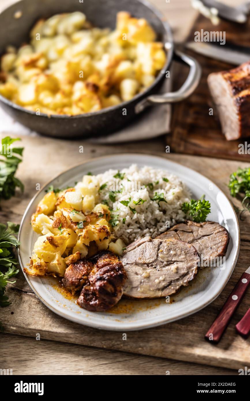A portion of baked juicy neck on a plate with a side dish of potatoes and rice and a sauce with baked goods. Stock Photo
