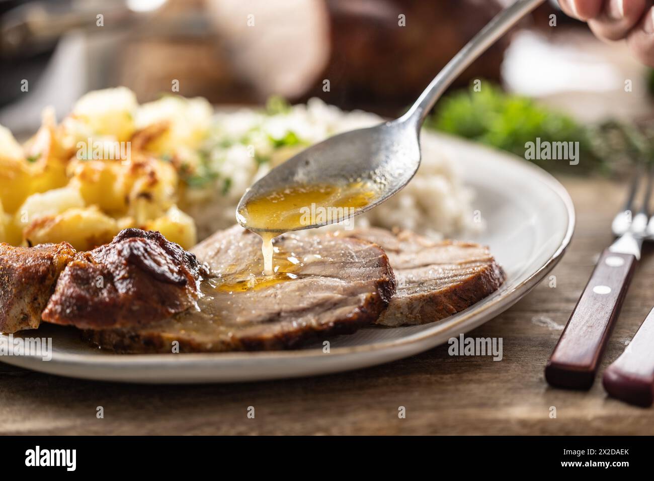 A close-up view of a spoon with sauce that pours over the meat, roasted neck. As a side dish to the meat are baked potatoes and jasmine rice. Stock Photo
