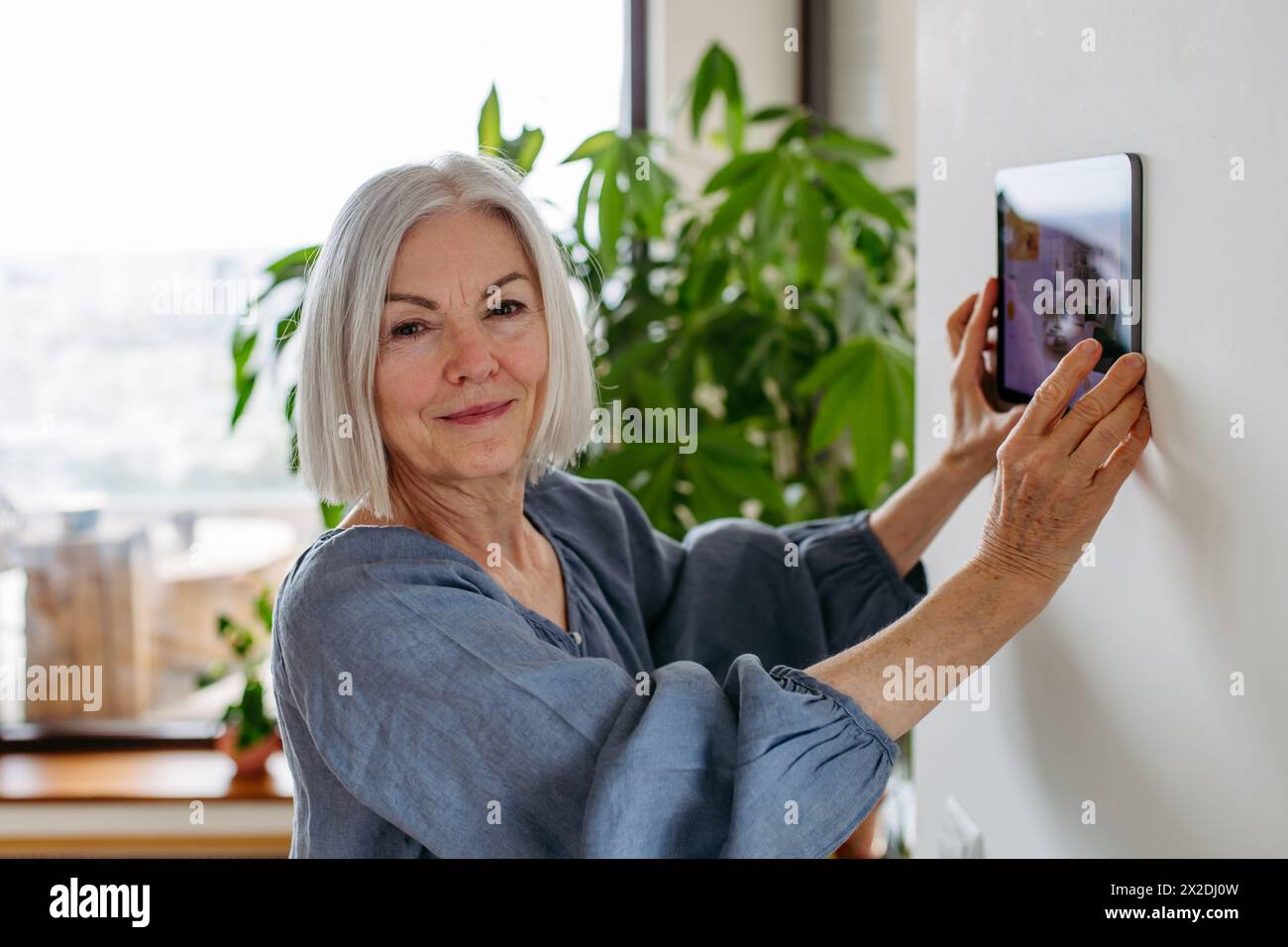 Mature woman adjusting household functions, lighting, security cameras, door locks, smart thermostat or heating settings. Sustainable and smart Stock Photo