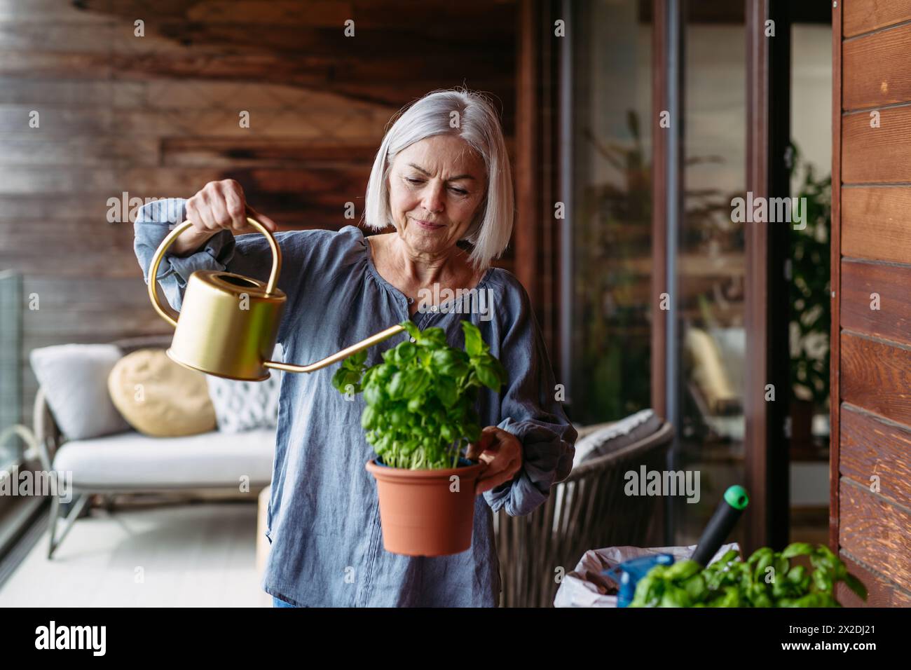 Portrait of beutiful mature woman taking care of plants on balcony. Spending free weekend at home. Stock Photo