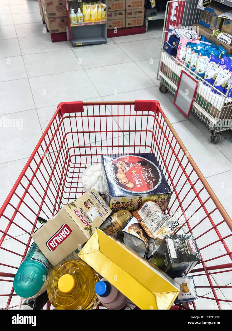Shopping cart filled with food and drinks and supermarket shelves in the background, grocery shopping concept. Bekasi, Indonesia, April 22, 2024 Stock Photo