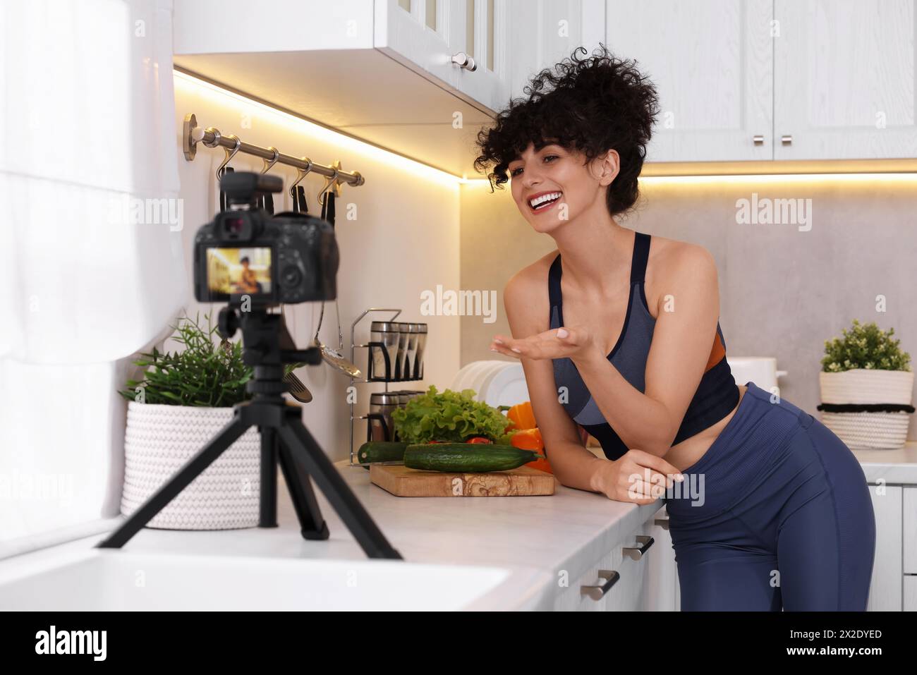 Smiling food blogger explaining something while recording video in kitchen Stock Photo