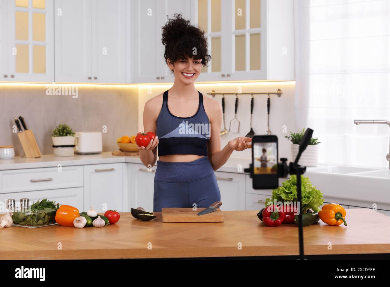 Smiling food blogger explaining something while recording video in kitchen Stock Photo
