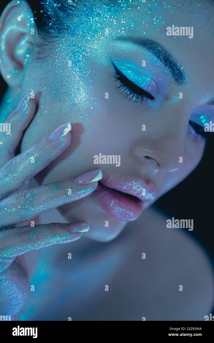 Woman cosmic themed glitter beauty makeup, highlighting eyes and cheeks under blue lighting Stock Photo