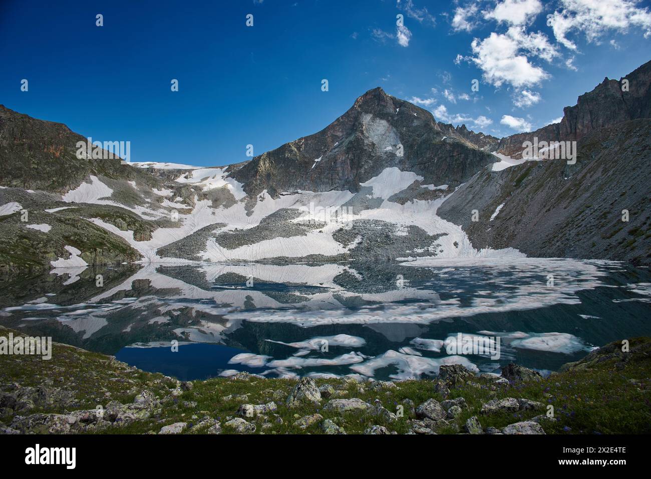Lake sits nestled amidst snow covered mountains under a clear blue sky Stock Photo