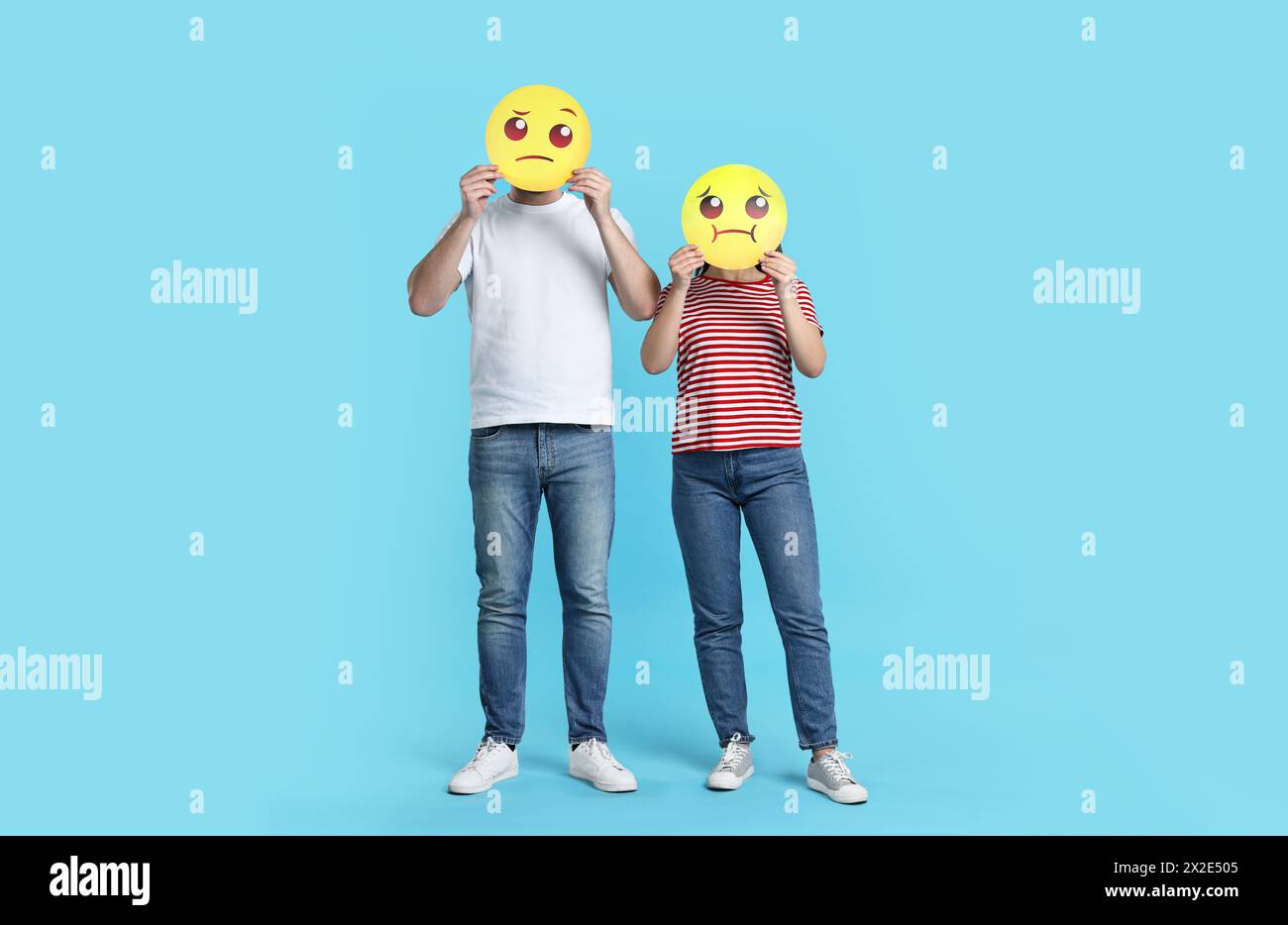 People covering faces with emoticons on light blue background Stock Photo