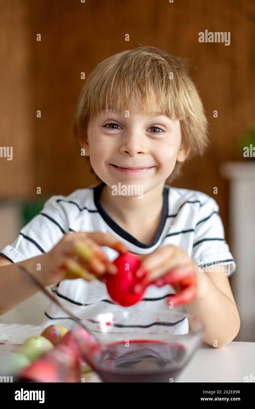 Beatiful blond child, boy, coloring and painting eggs for Easter at home, preparing for the holidays Stock Photo