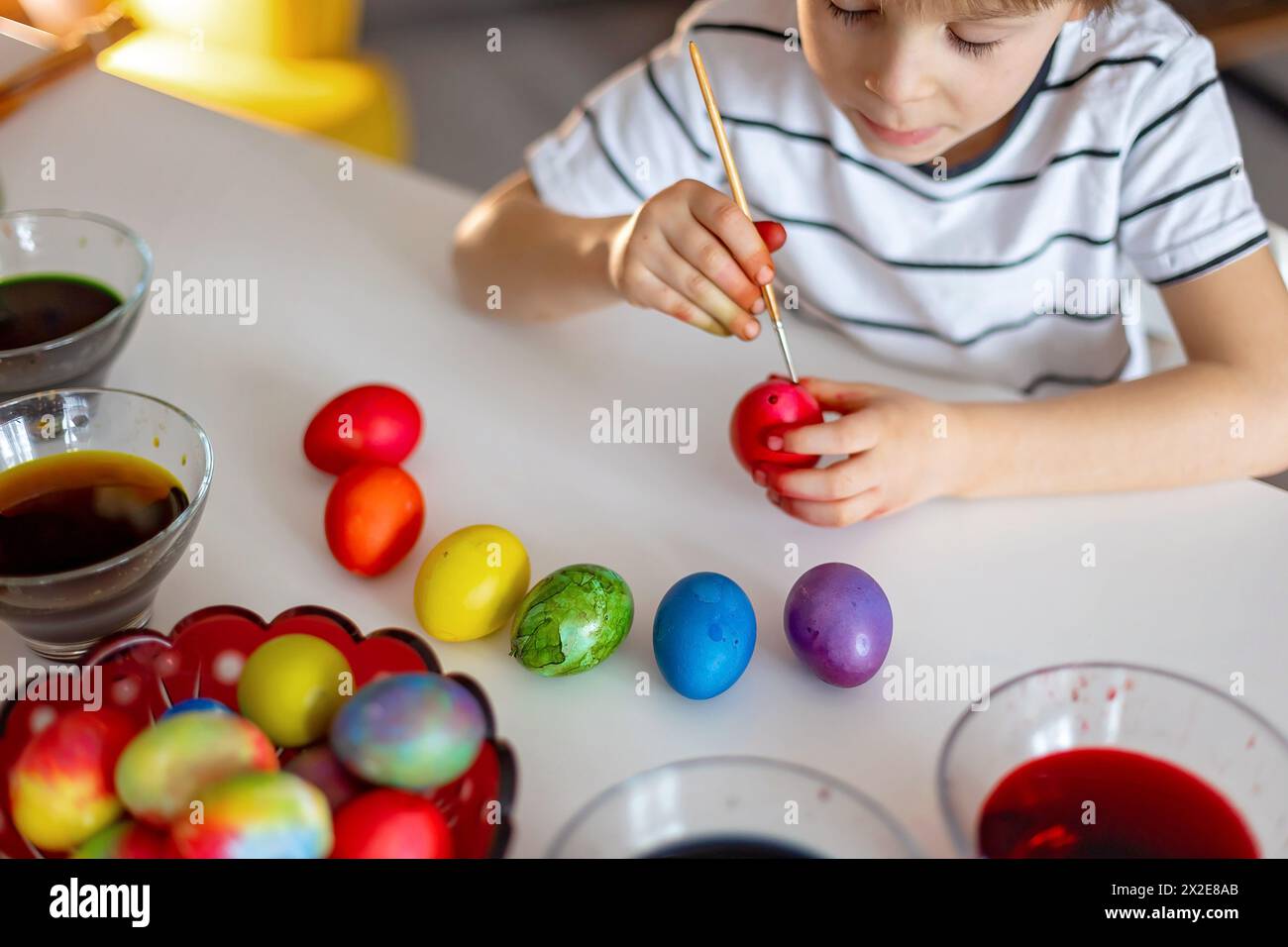 Beatiful blond child, boy, coloring and painting eggs for Easter at home, preparing for the holidays Stock Photo