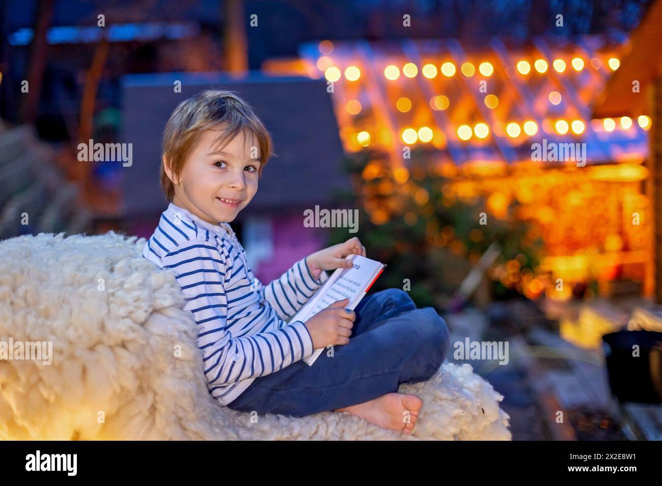 Beautiful blond child, boy, reading a book at night with flashligh, sitting on the stairs in garden in cottage village house Stock Photo