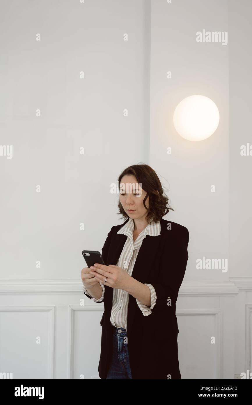 Half-Asian woman in business casual attire looks at phone Stock Photo