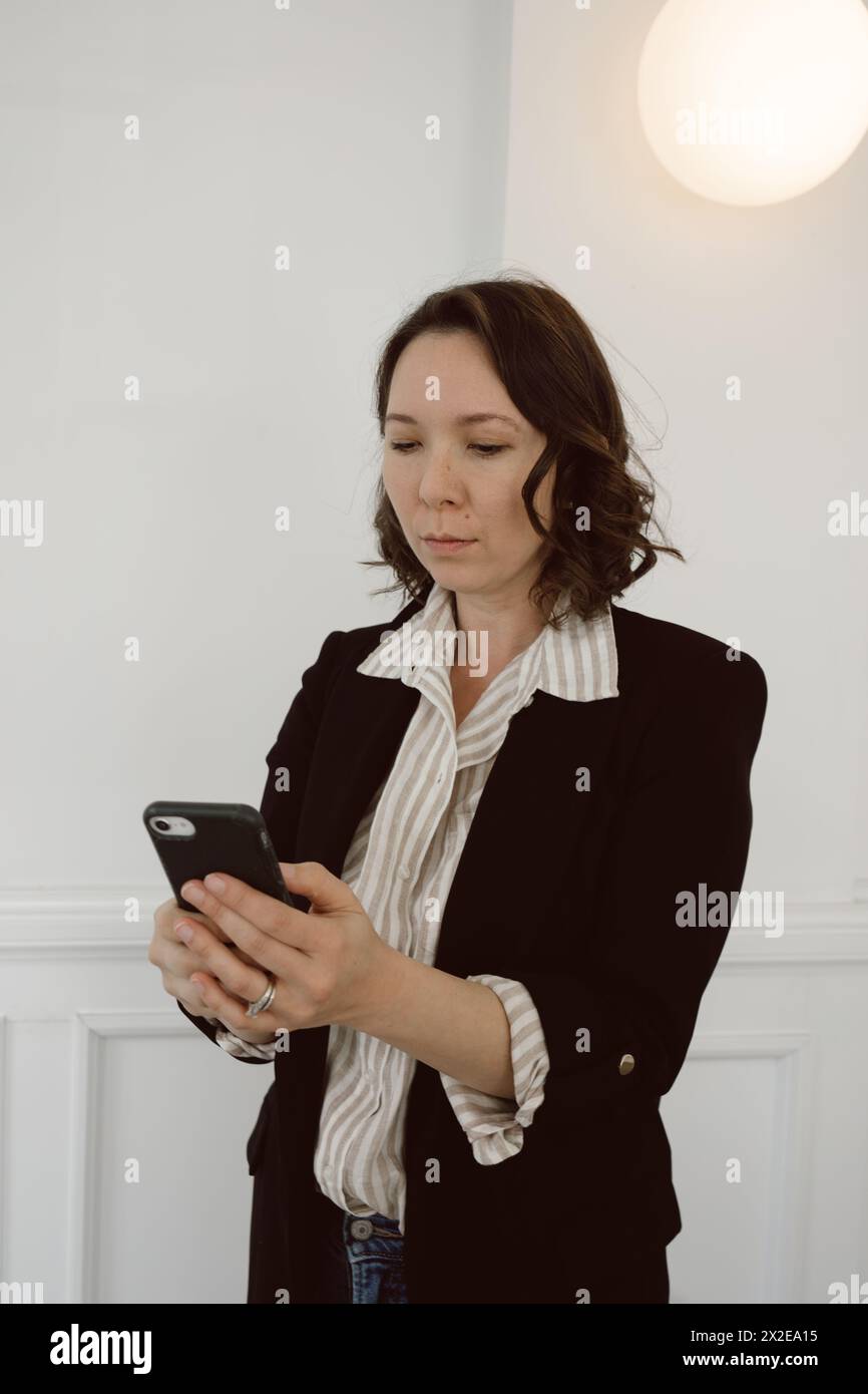 Mixed race woman in business casual attire looks at phone Stock Photo