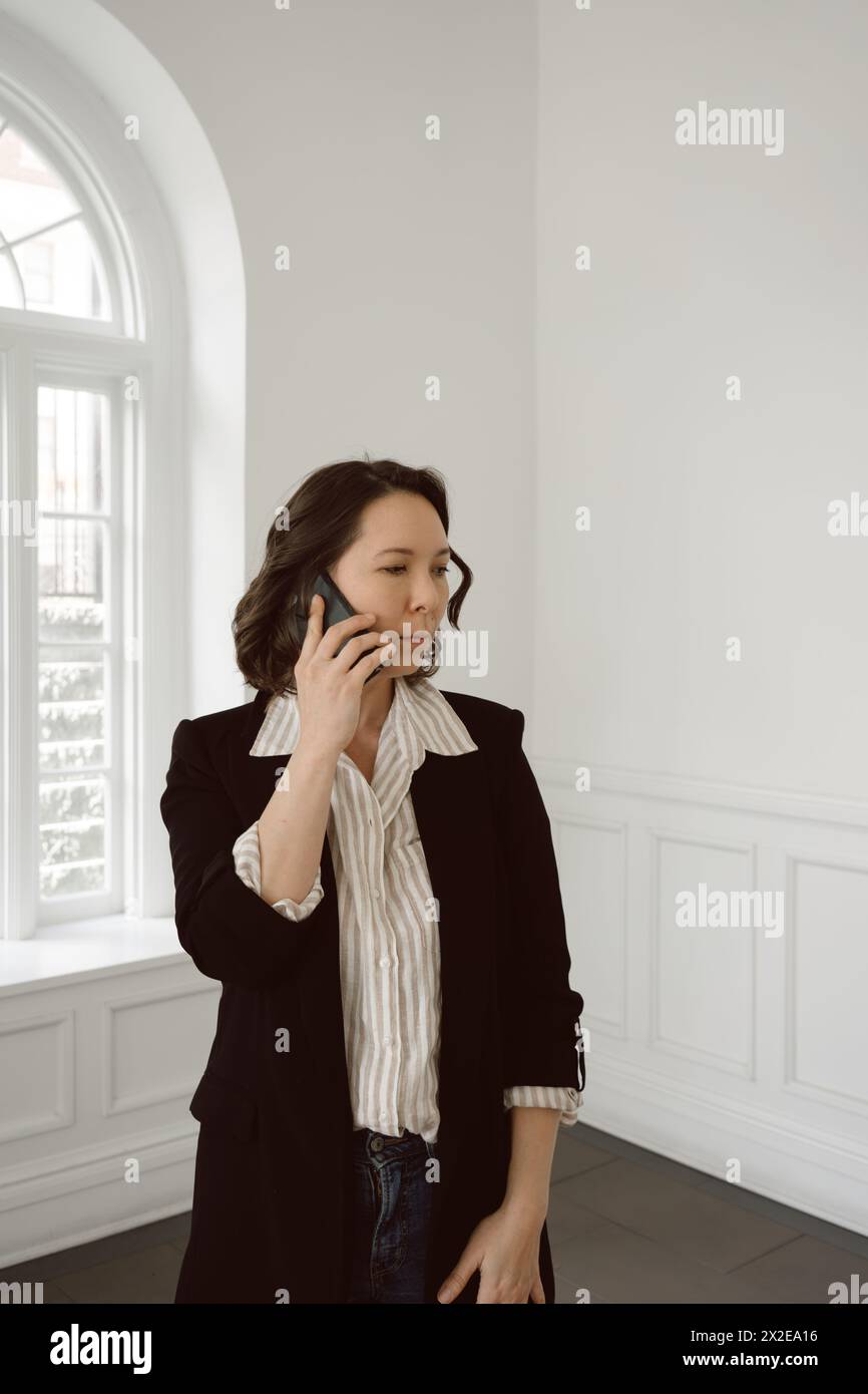 Mixed race woman in business casual attire talks on mobile phone Stock Photo