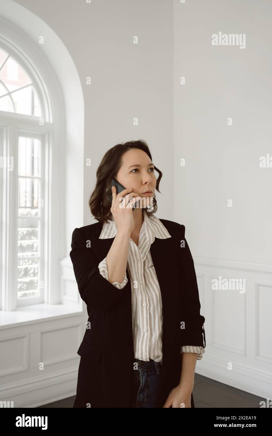 Half-Asian woman talks on phone in business casual attire Stock Photo