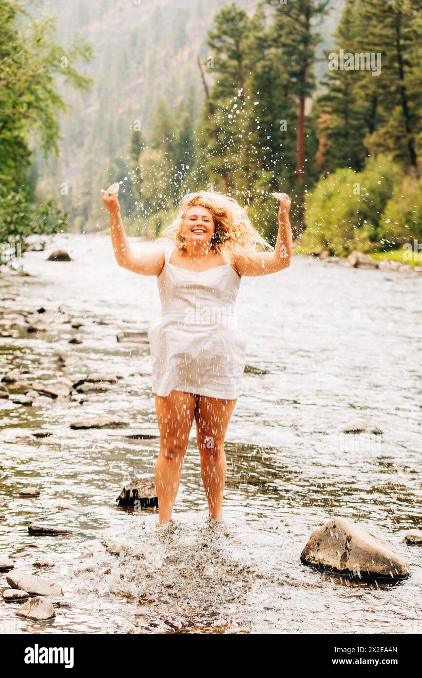 Joyful teenage girl in white sundress jumping for joy in river Stock Photo