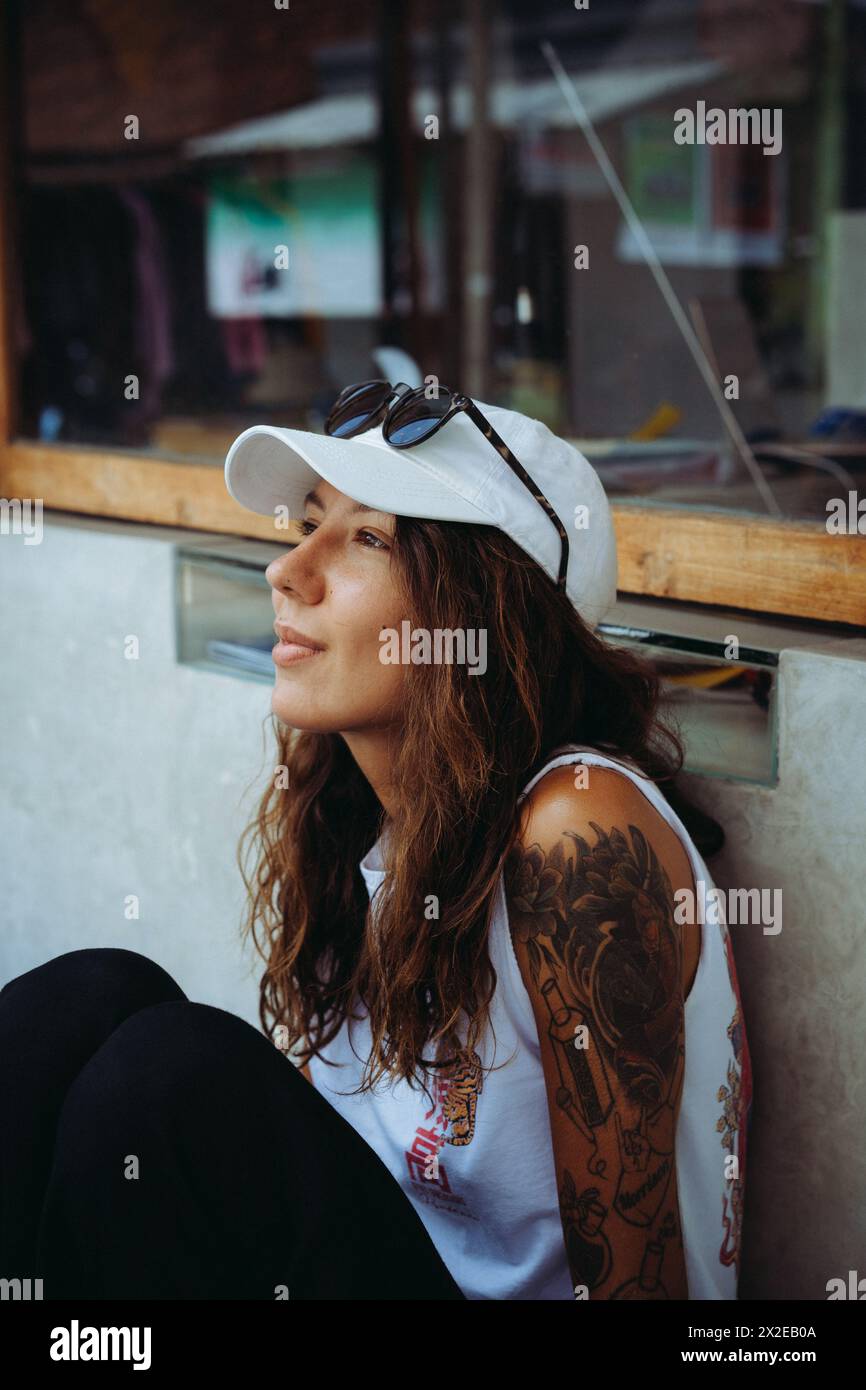 Young smiling tattooed woman sitting on a bench, street photo. Stock Photo