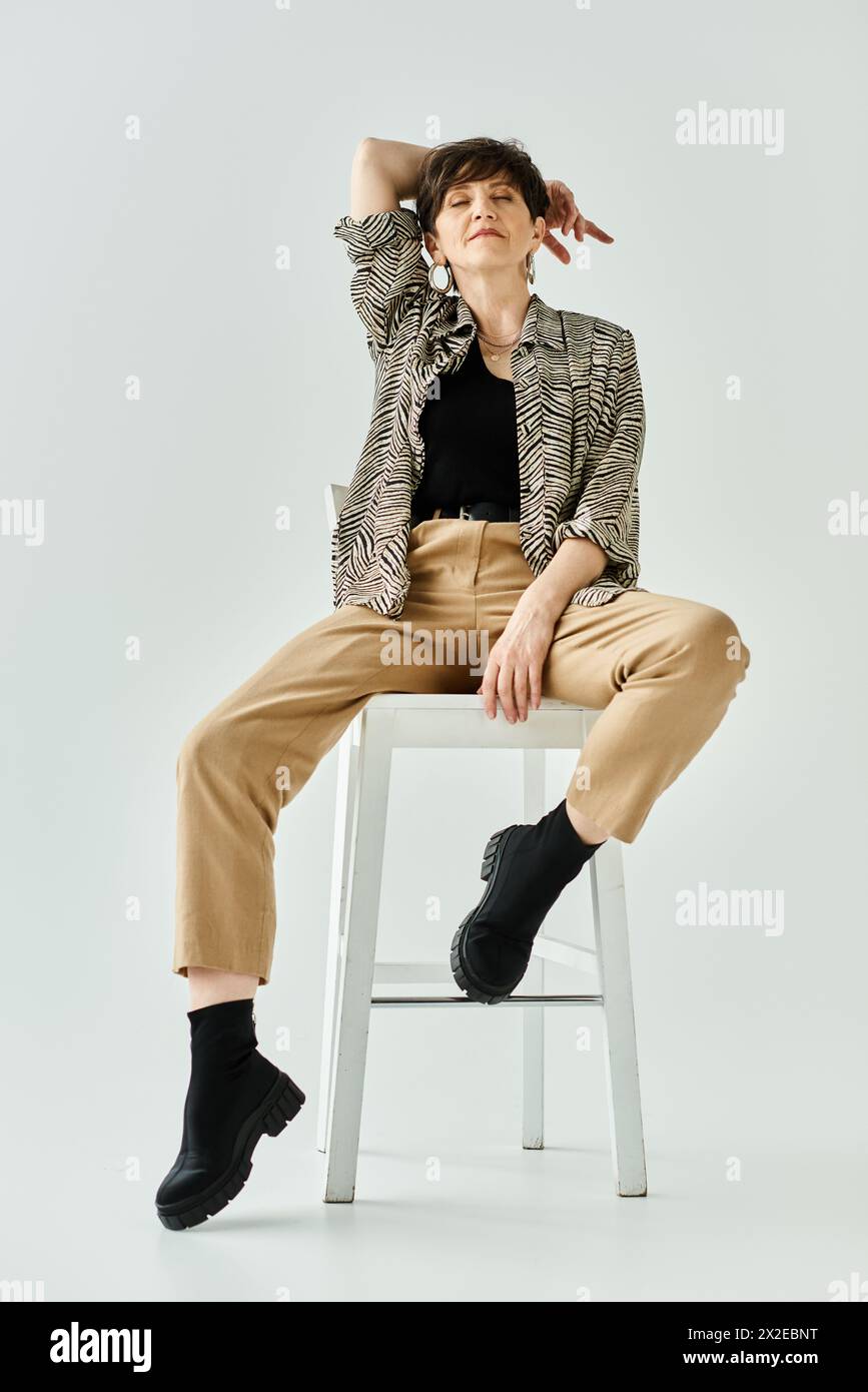 A middle-aged woman with short hair, dressed in stylish attire, sits on a stool posing gracefully for a portrait. Stock Photo