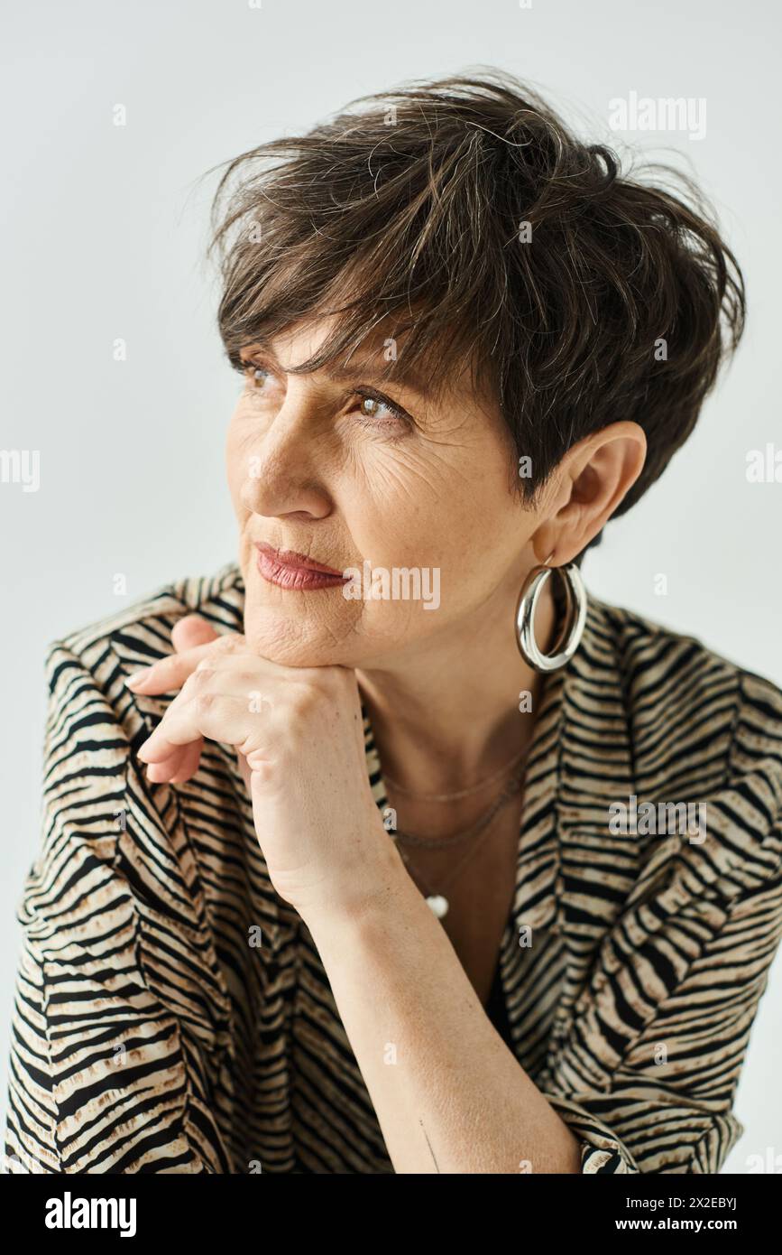 Middle-aged woman with short hair wearing a black and white shirt exudes elegance in a studio setting. Stock Photo