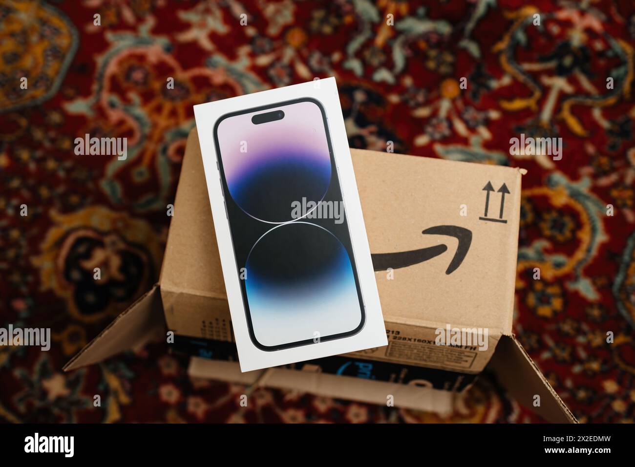 London, United Kingdom - Sep 29, 2022: Unboxing the latest Apple iPhone 14 Pro from an Amazon cardboard box, featuring the smiling arrow logo, set against a rug in a living room. Stock Photo