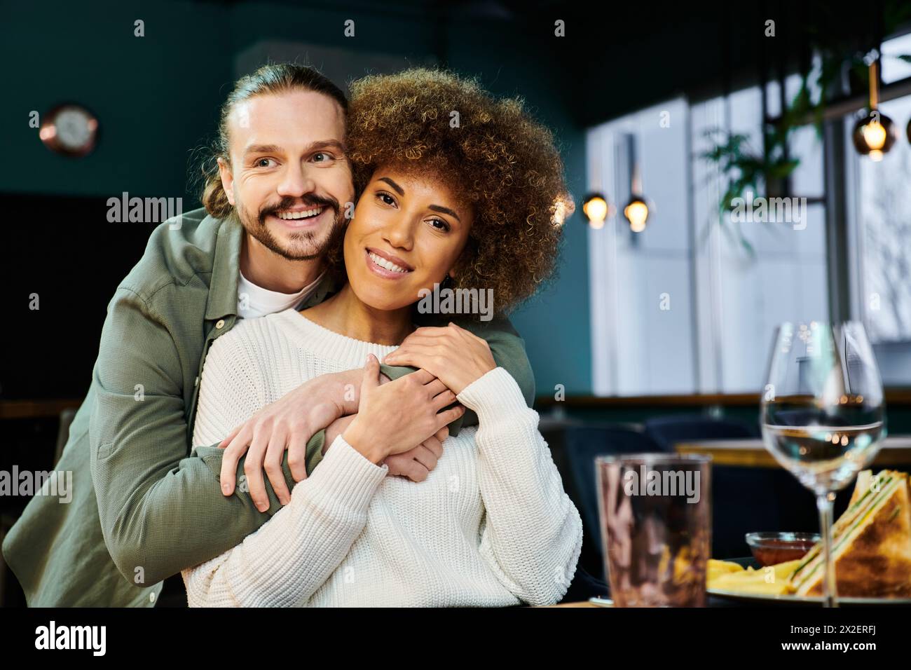 An African American woman and man share a tender hug in a modern cafe setting. Stock Photo