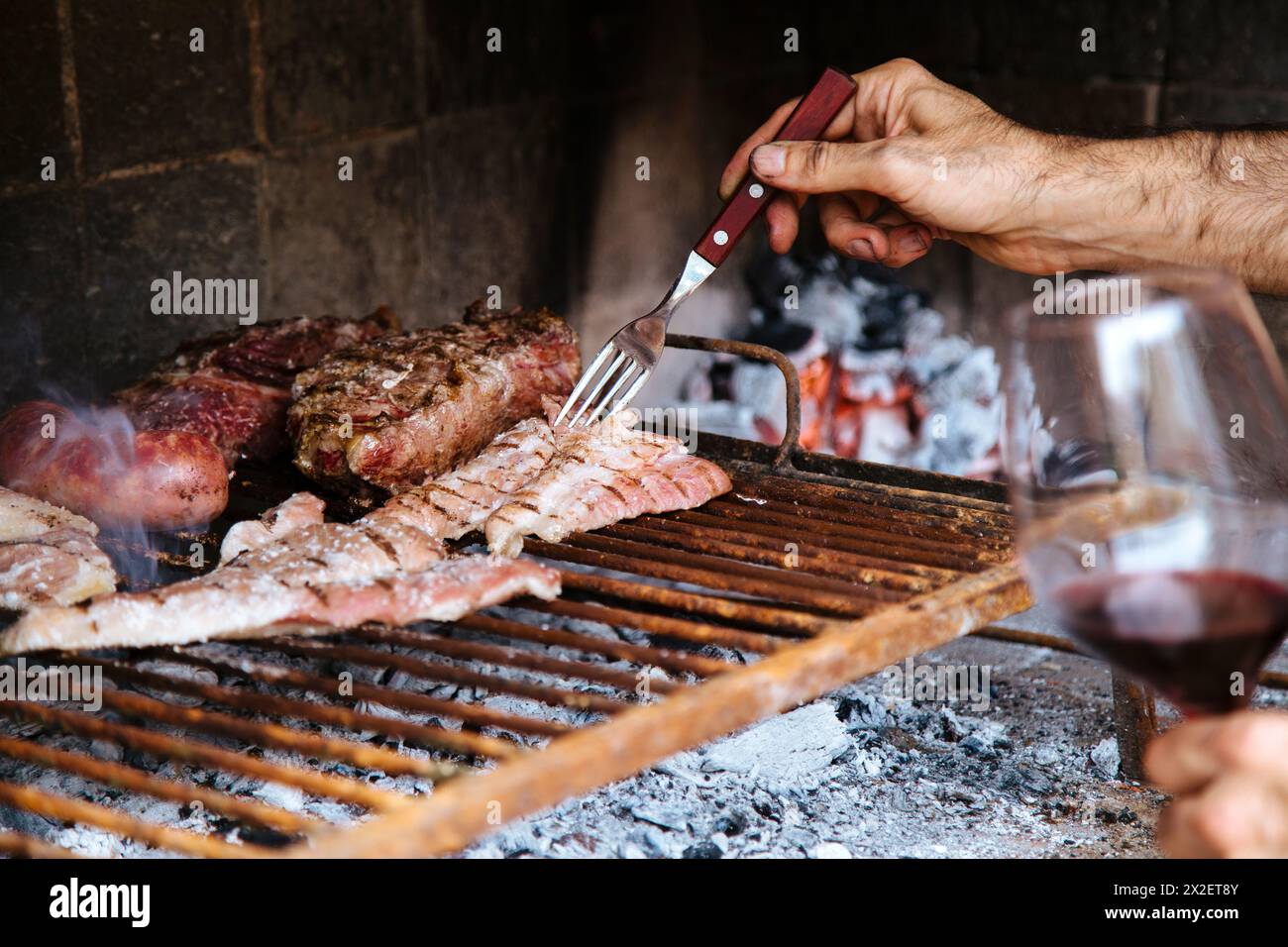 Man with a red wine cup making a barbeque, bbq meat cooking on grill. Traditional Asado of Argentina, Paraguay y Uruguay. Stock Photo