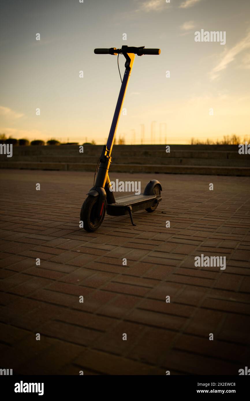 Electric Scooter Standing Alone a Calm Evening. A solitary electric scooter is captured as dusk settles, casting a warm glow Stock Photo