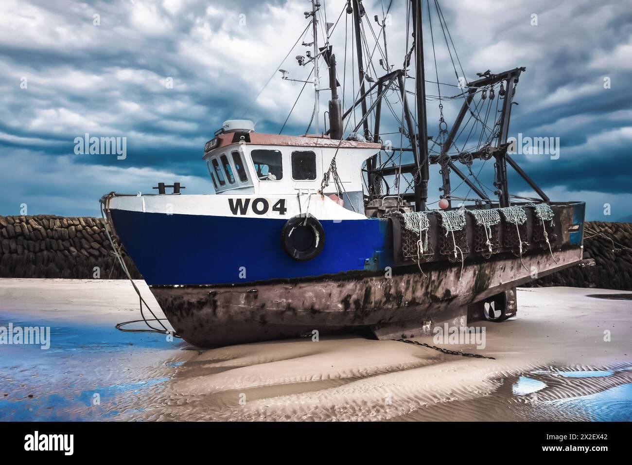 Blue Fishing boat moored in Folkestone harbour at low tide with dark ...