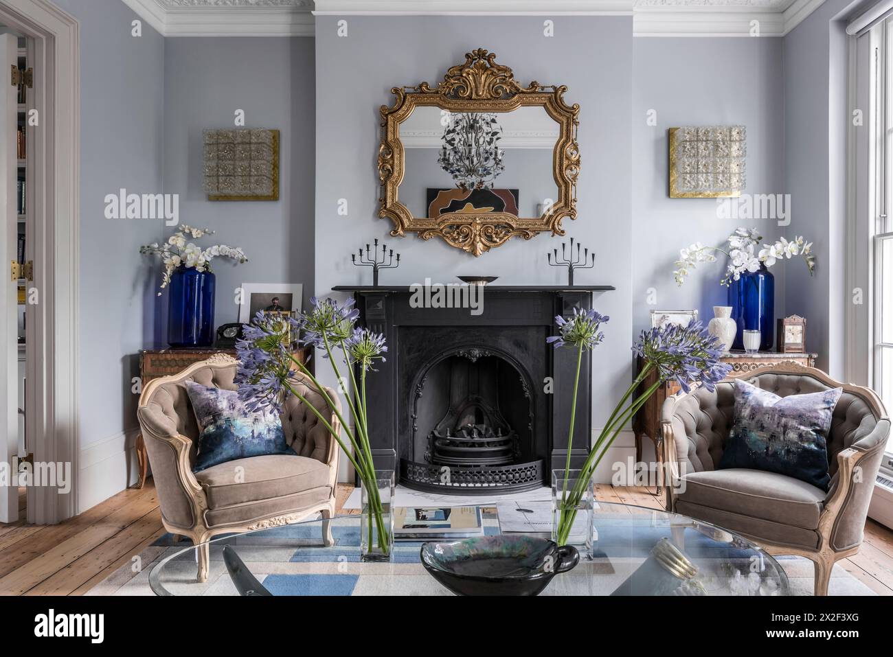 Antique gilt framed mirror above fireplace with beige armchairs in Georgian townhouse, Paultons Square, Chelsea, London, UK. Stock Photo