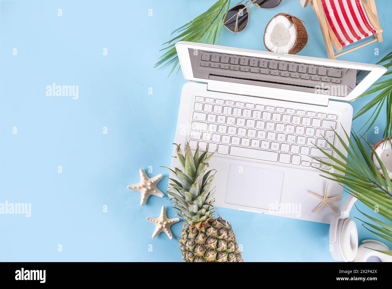 Work and vacation. Creative summer beach office flat lay with white laptop, tropical summer accessories, palm tree leaves, sunglasses, flip flops, pin Stock Photo