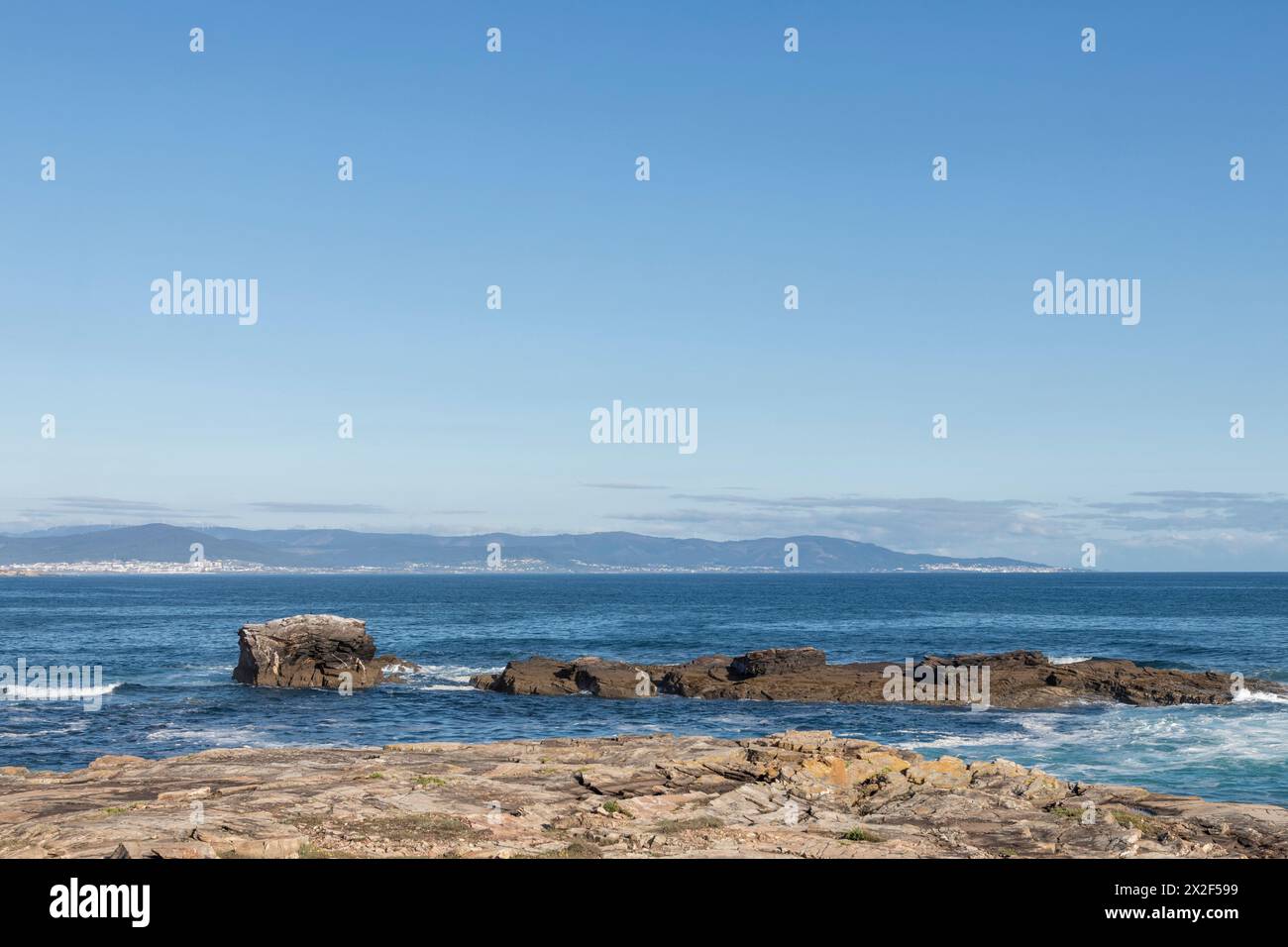 peaceful coastal landscape with a rocky shore, calm sea, and distant mountains under a clear sky Stock Photo